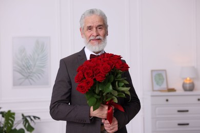 Photo of Senior man with bouquet of red roses at home