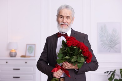 Photo of Senior man with bouquet of red roses at home