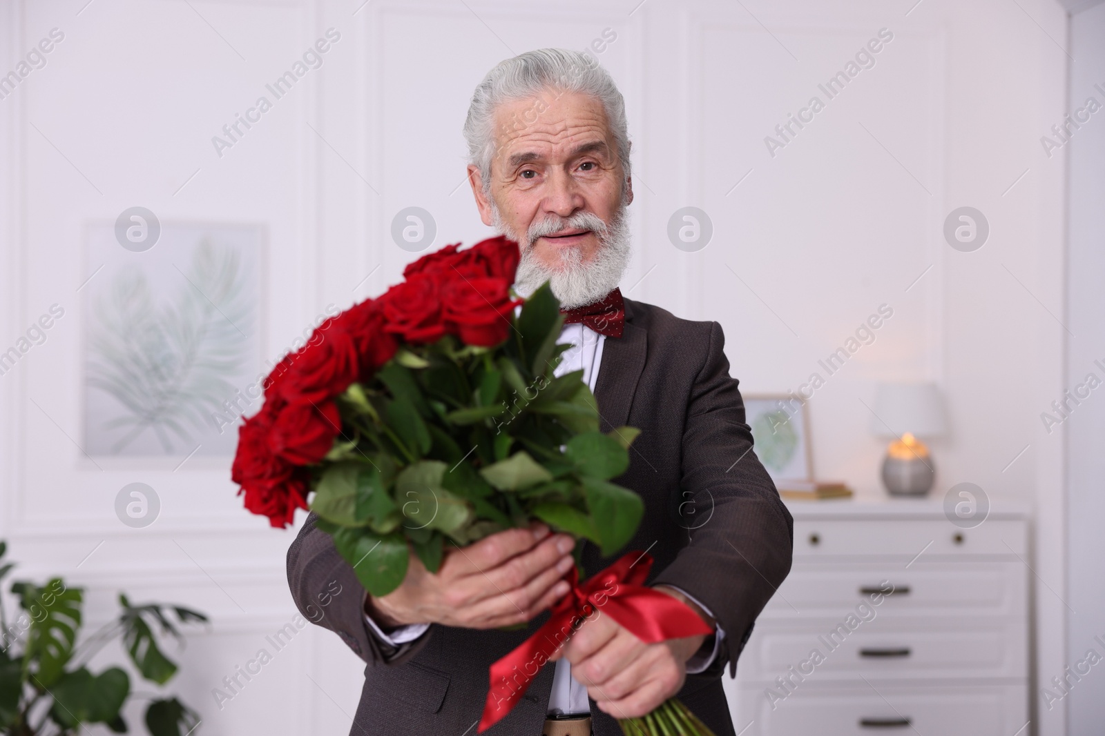 Photo of Senior man with bouquet of red roses at home