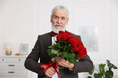 Photo of Senior man with bouquet of red roses at home