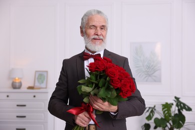 Photo of Senior man with bouquet of red roses at home