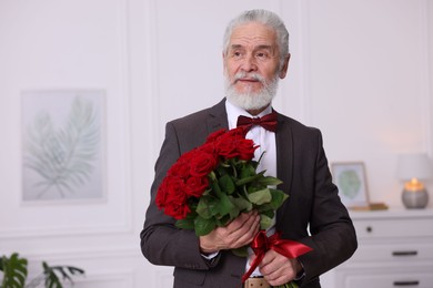 Photo of Senior man with bouquet of red roses at home