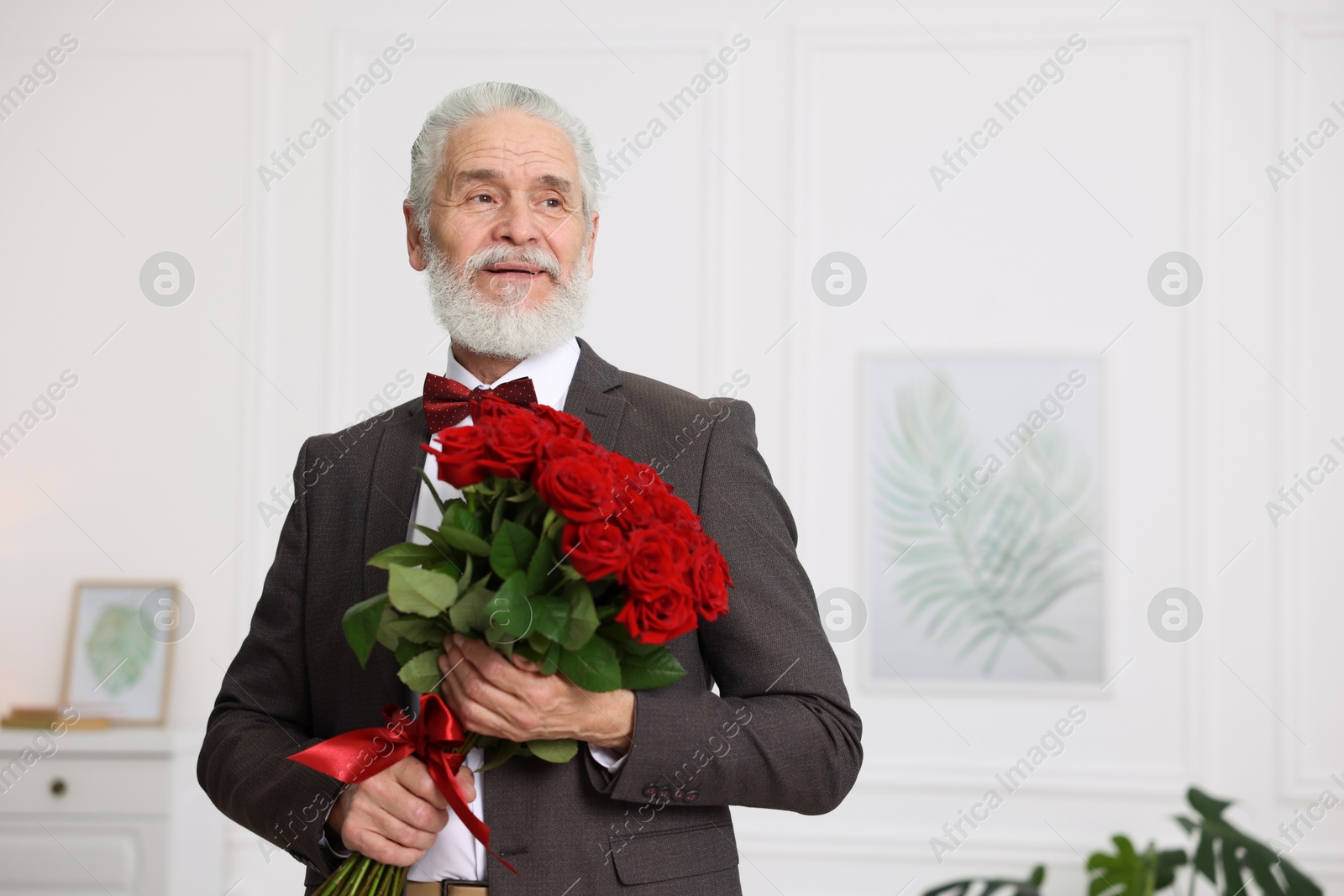 Photo of Senior man with bouquet of red roses at home, space for text