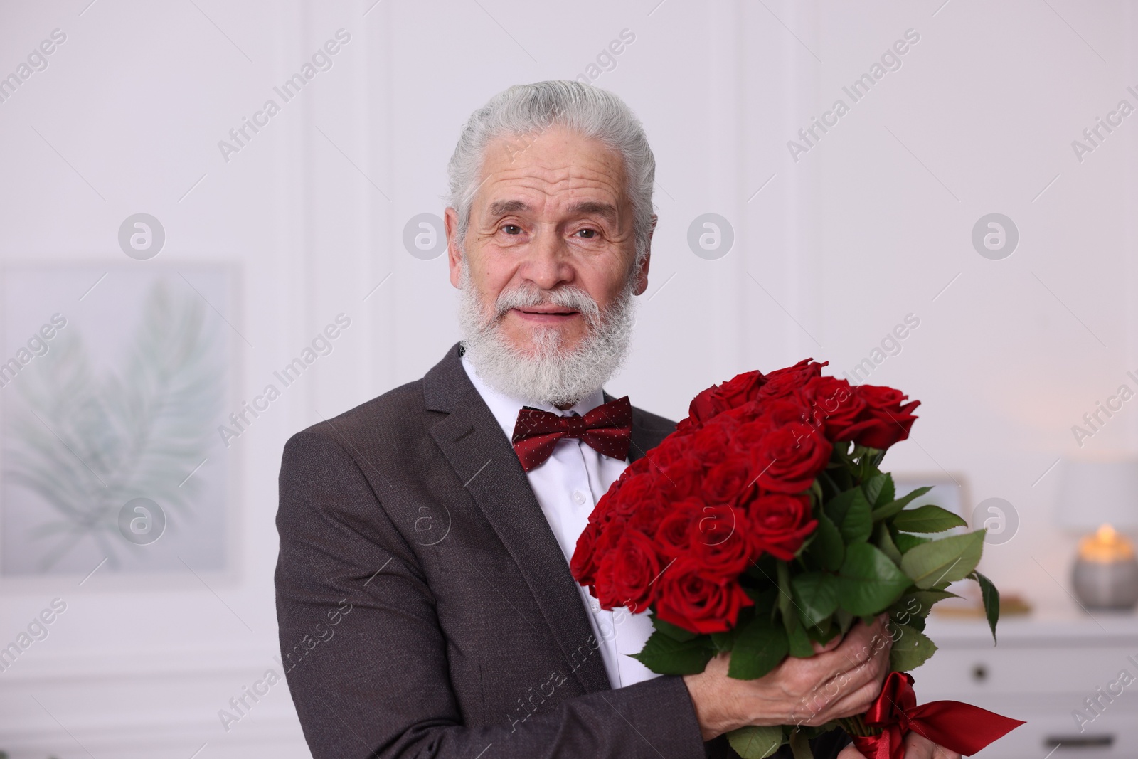 Photo of Senior man with bouquet of red roses at home