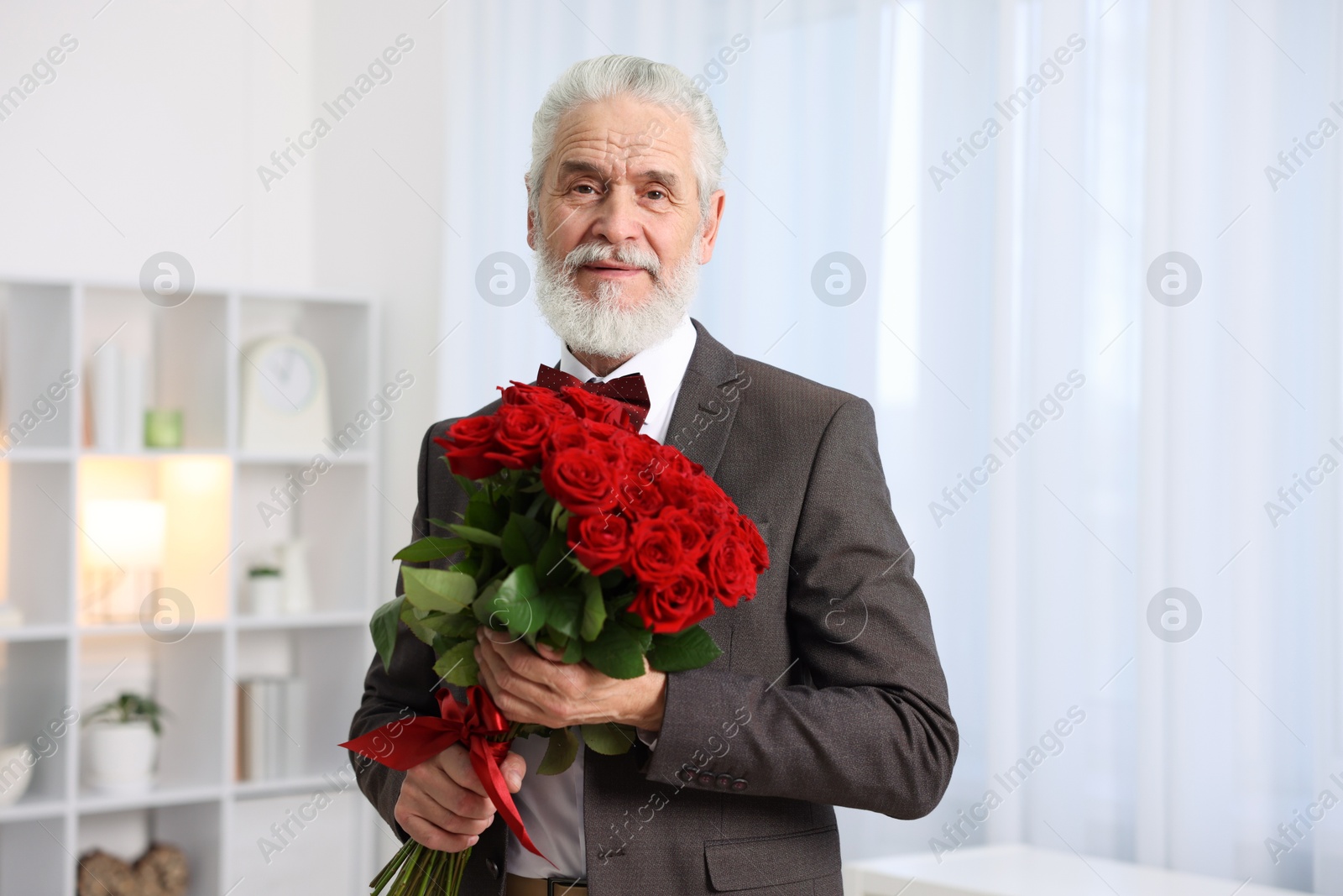 Photo of Senior man with bouquet of red roses at home