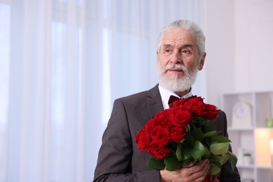 Photo of Senior man with bouquet of red roses at home, space for text