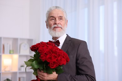 Photo of Senior man with bouquet of red roses at home