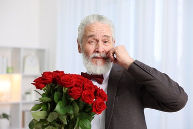 Photo of Senior man with bouquet of red roses at home