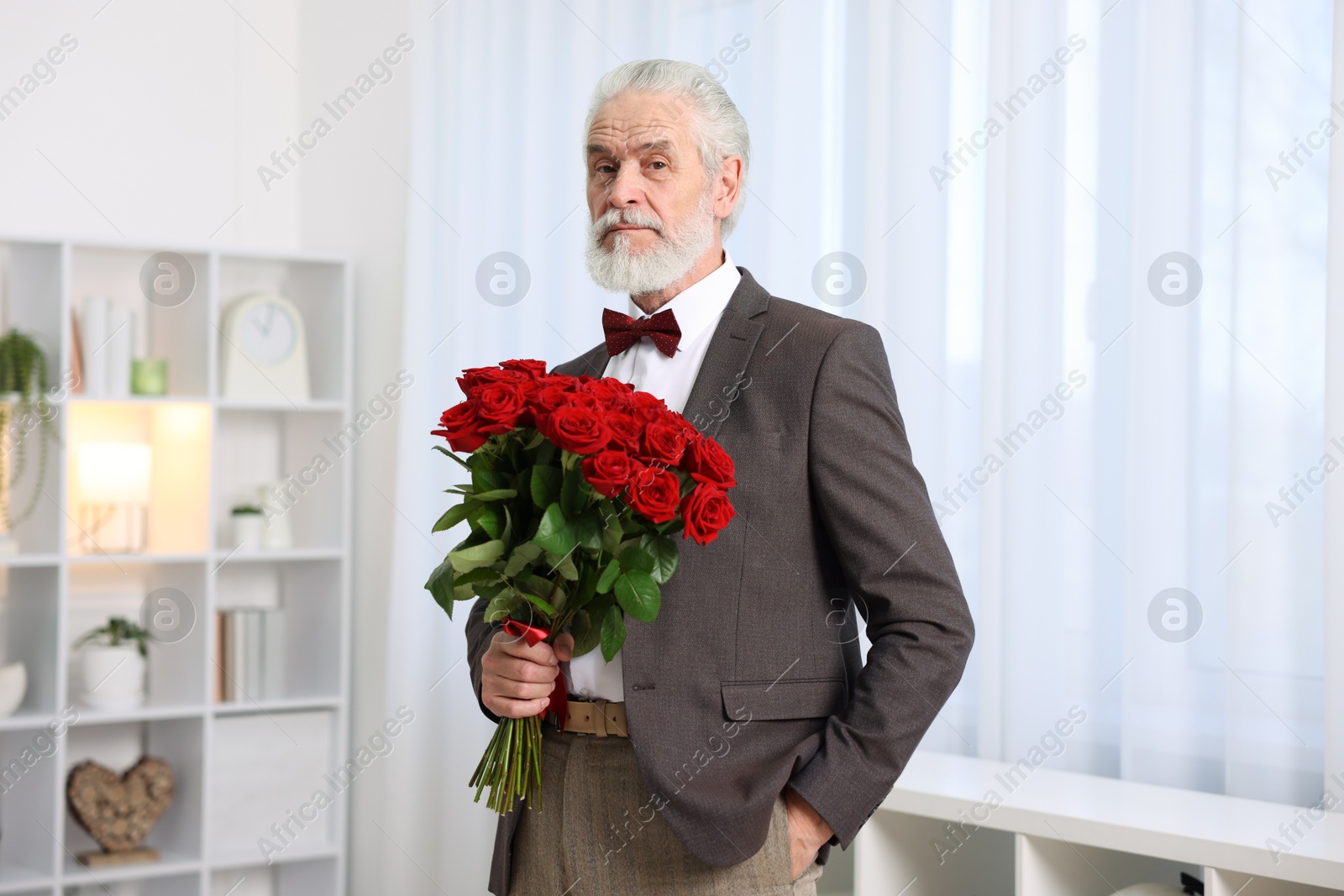 Photo of Senior man with bouquet of red roses at home