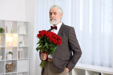 Photo of Senior man with bouquet of red roses at home