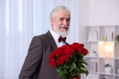 Photo of Senior man with bouquet of red roses at home