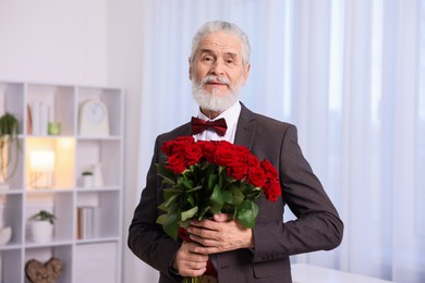 Photo of Senior man with bouquet of red roses at home