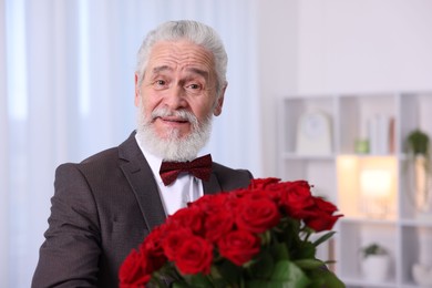 Photo of Senior man with bouquet of red roses at home