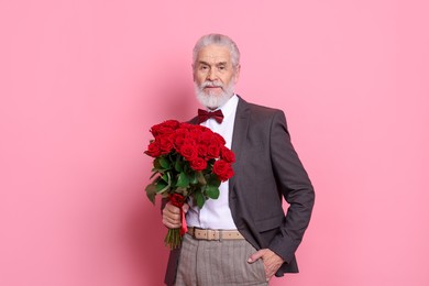 Photo of Senior man with bouquet of red roses on pink background