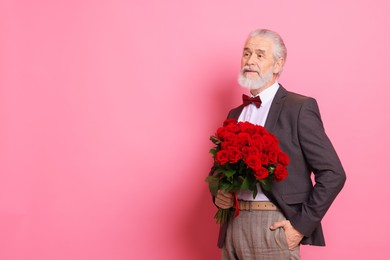 Photo of Senior man with bouquet of red roses on pink background, space for text