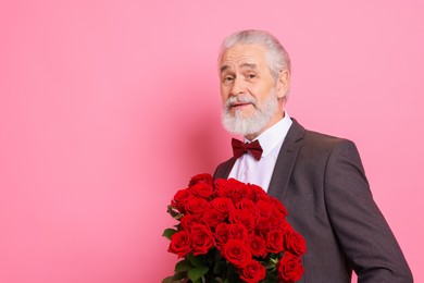 Photo of Senior man with bouquet of red roses on pink background, space for text