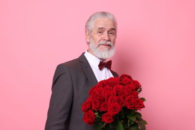 Photo of Senior man with bouquet of red roses on pink background