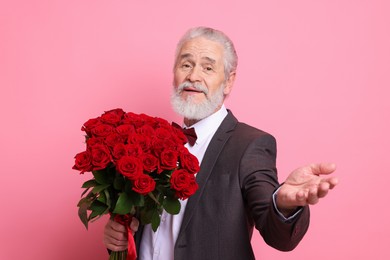 Photo of Senior man with bouquet of red roses on pink background