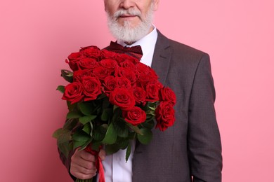 Photo of Senior man with bouquet of red roses on pink background, closeup