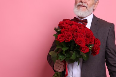 Photo of Senior man with bouquet of red roses on pink background, closeup. Space for text