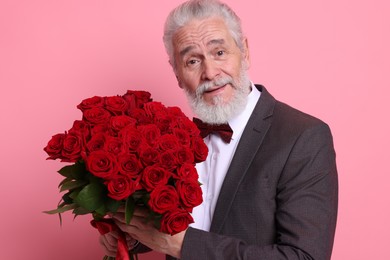 Photo of Senior man with bouquet of red roses on pink background