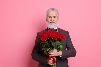 Photo of Senior man with bouquet of red roses on pink background