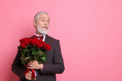 Photo of Senior man with bouquet of red roses on pink background, space for text