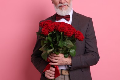 Photo of Senior man with bouquet of red roses on pink background, closeup