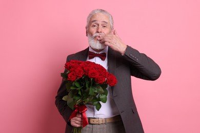 Photo of Senior man with bouquet of red roses on pink background