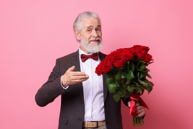 Photo of Senior man with bouquet of red roses on pink background