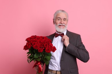 Photo of Senior man with bouquet of red roses on pink background