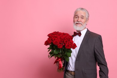 Photo of Senior man with bouquet of red roses on pink background, space for text