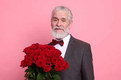 Photo of Senior man with bouquet of red roses on pink background