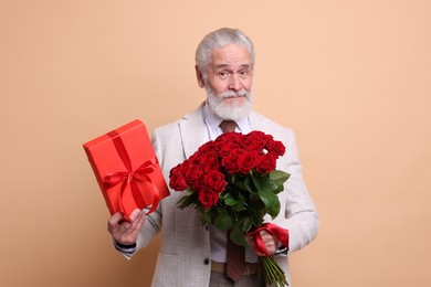 Photo of Senior man with bouquet of red roses and gift box on beige background