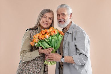 Photo of Happy couple with bouquet of tulips on beige background