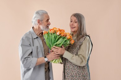 Photo of Happy couple with bouquet of tulips on beige background