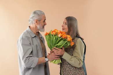 Photo of Lovely couple with bouquet of tulips on beige background