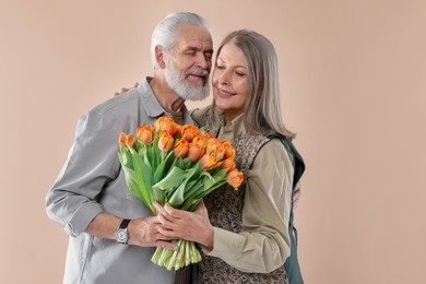 Photo of Happy couple with bouquet of tulips on beige background