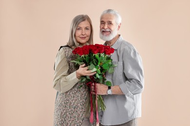 Photo of Happy couple with bouquet of red roses on beige background