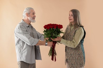 Photo of Man presenting bouquet of red roses to his happy wife on beige background