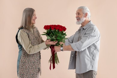 Photo of Man presenting bouquet of red roses to his happy wife on beige background