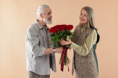 Photo of Man presenting bouquet of red roses to his happy wife on beige background