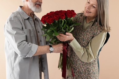 Photo of Man presenting bouquet of red roses to his happy wife on beige background, closeup