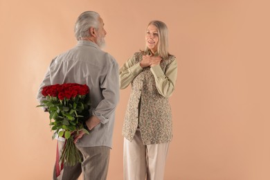 Photo of Man hiding bouquet of red roses for his happy wife on beige background, back view