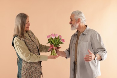 Photo of Man presenting bouquet of pink tulips to his wife on beige background