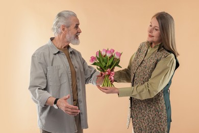 Photo of Man presenting bouquet of pink tulips to his wife on beige background