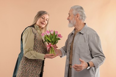 Photo of Man presenting bouquet of pink tulips to his happy wife on beige background