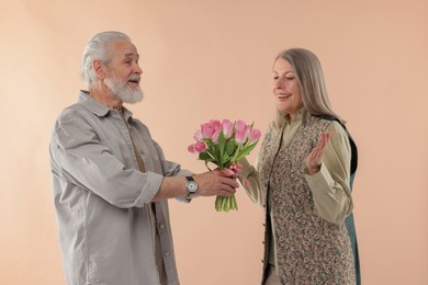 Photo of Man presenting bouquet of pink tulips to his happy wife on beige background