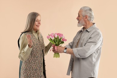 Photo of Man presenting bouquet of pink tulips to his happy wife on beige background