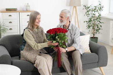 Photo of Happy couple with bouquet of red roses on sofa at home